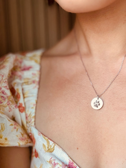 Custom pendant necklace with a paw print pendant worn by a person in a floral dress.