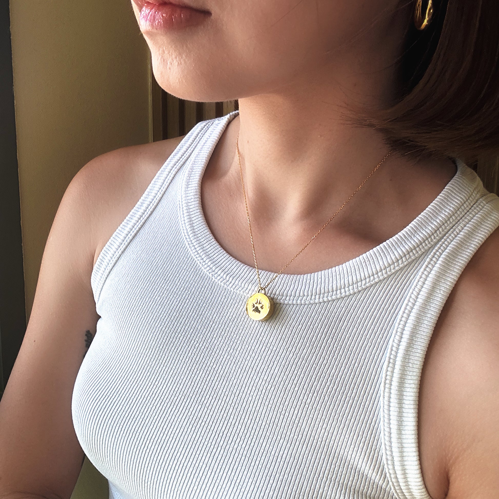 Person wearing a white tank top with a gold keepsake pendant necklace featuring a paw print.