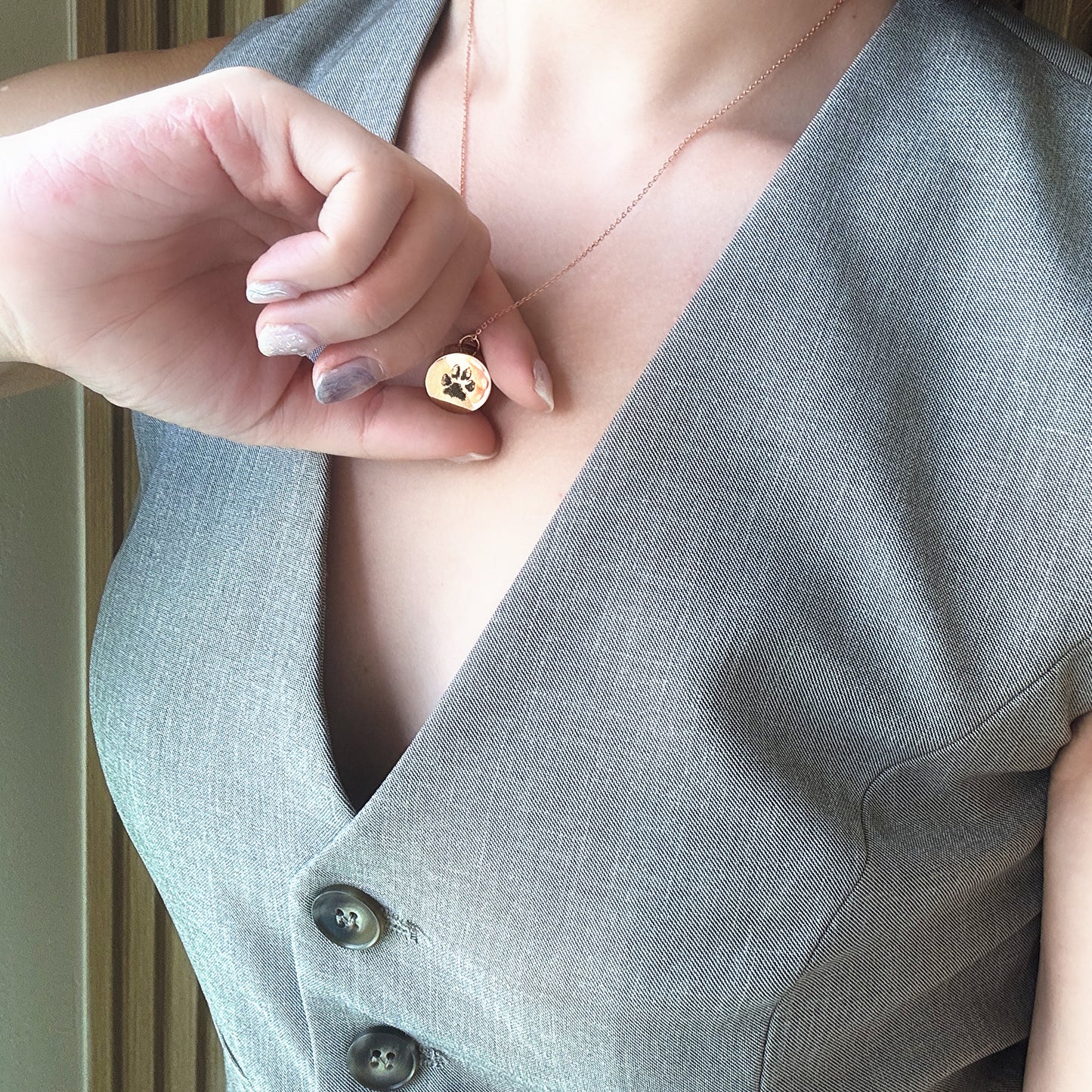 Person wearing a gray vest with a rose gold keepsake pendant