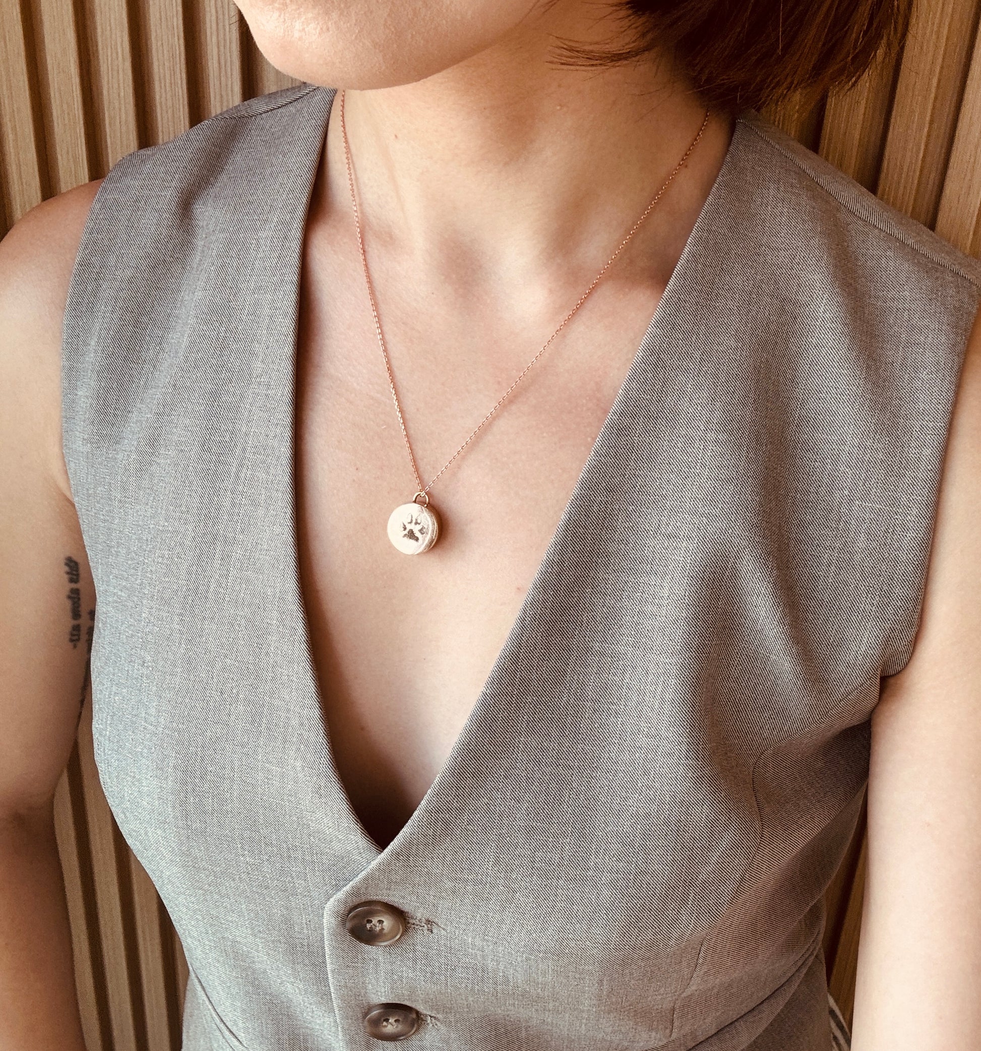 Person wearing a light gray vest with a rose gold keepsake pendant necklace, against a neutral background